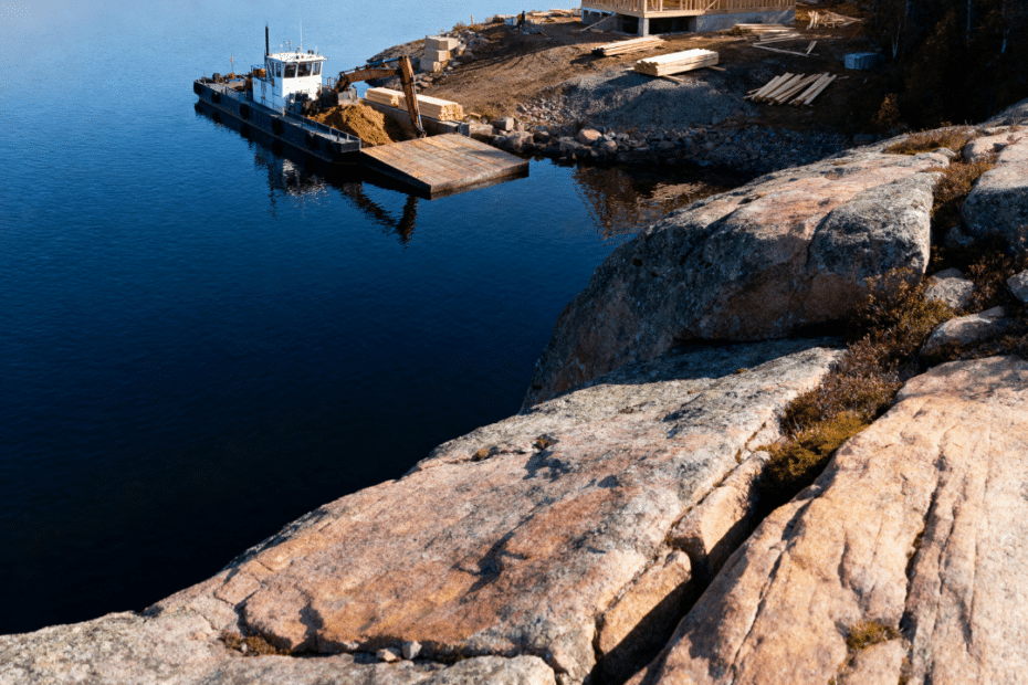 Island cottage builders Muskoka project showing barge-access construction on a granite shoreline of the Canadian Shield during daylight